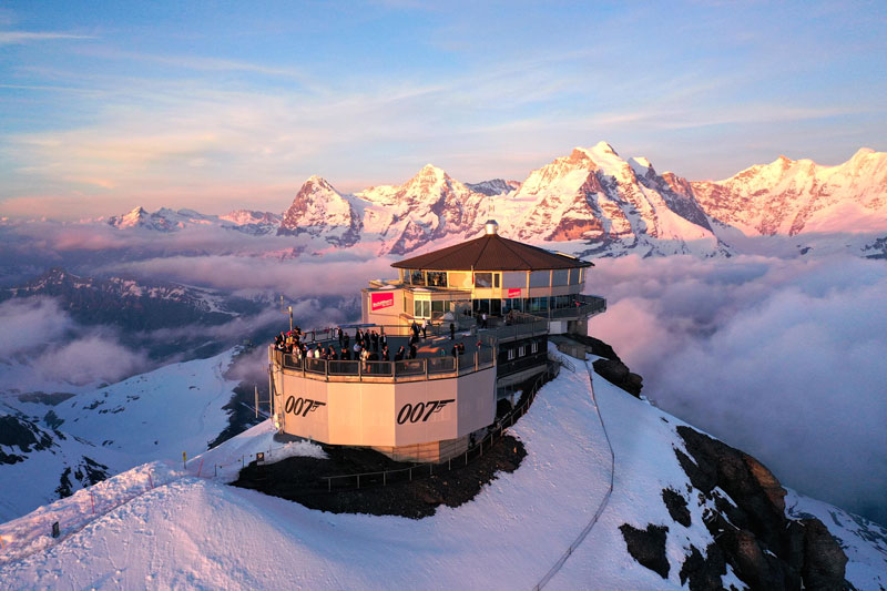 Tourists on viewing platform at summit of Schilthorn Piz Gloria at sunset.